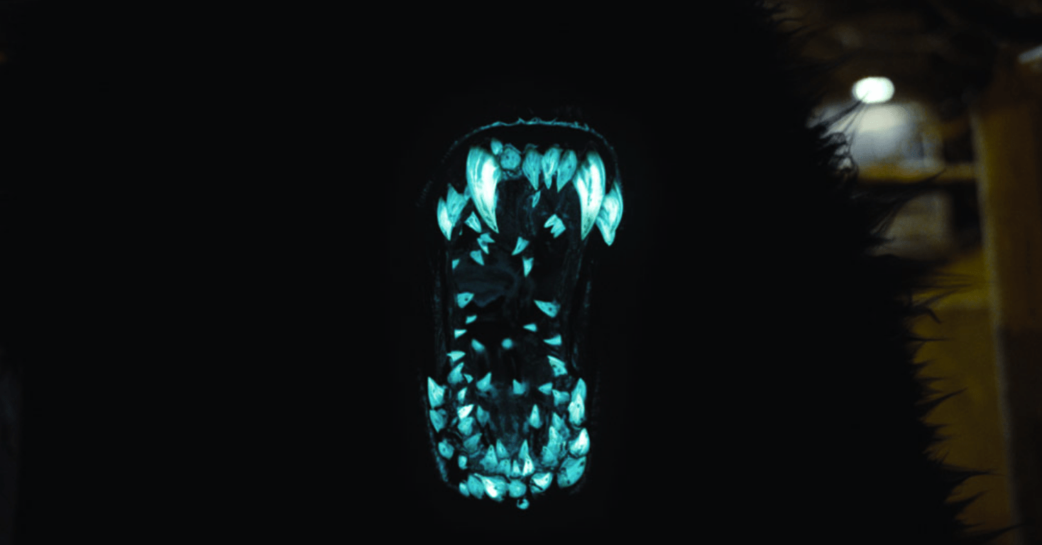 Uma boca cheia de dentes azuis brilhantes na mandíbula de um monstro peludo de jato preto.