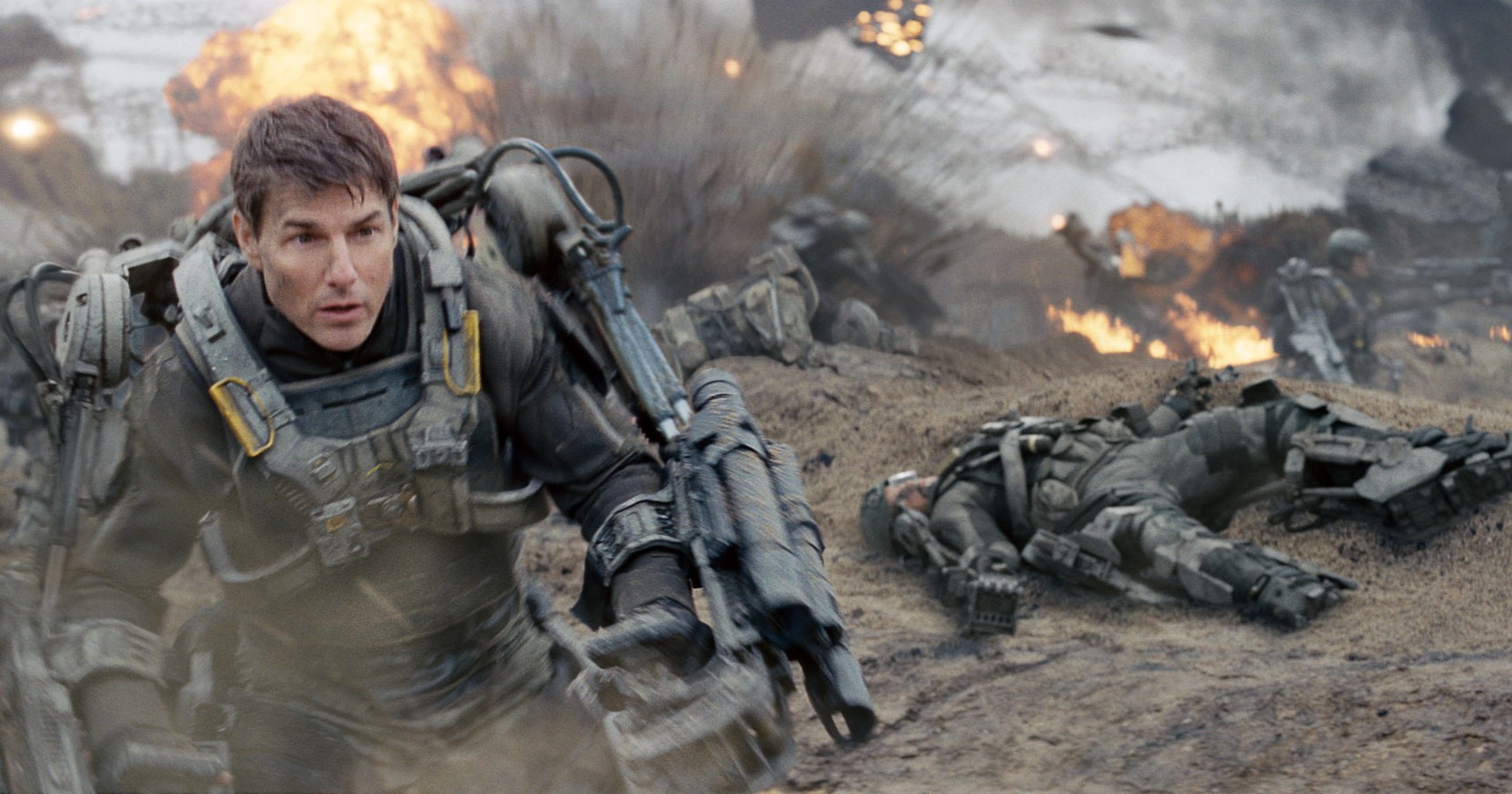 Tom Cruise como gaiola em armadura de força invadindo uma praia cheia de explosões em Edge of Tomorrow.