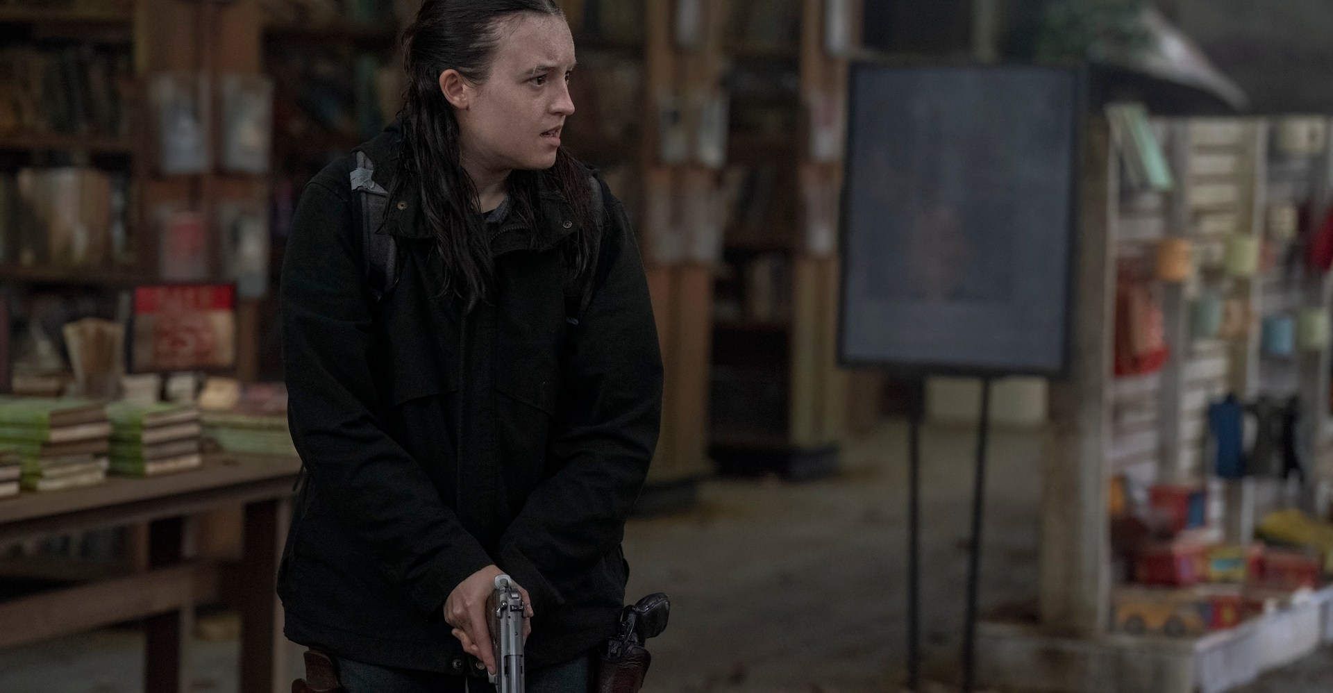 Ellie do último show de nós fica em uma biblioteca degradada, segurando uma arma Ellie do último show de nós fica em uma biblioteca degradada, segurando uma arma