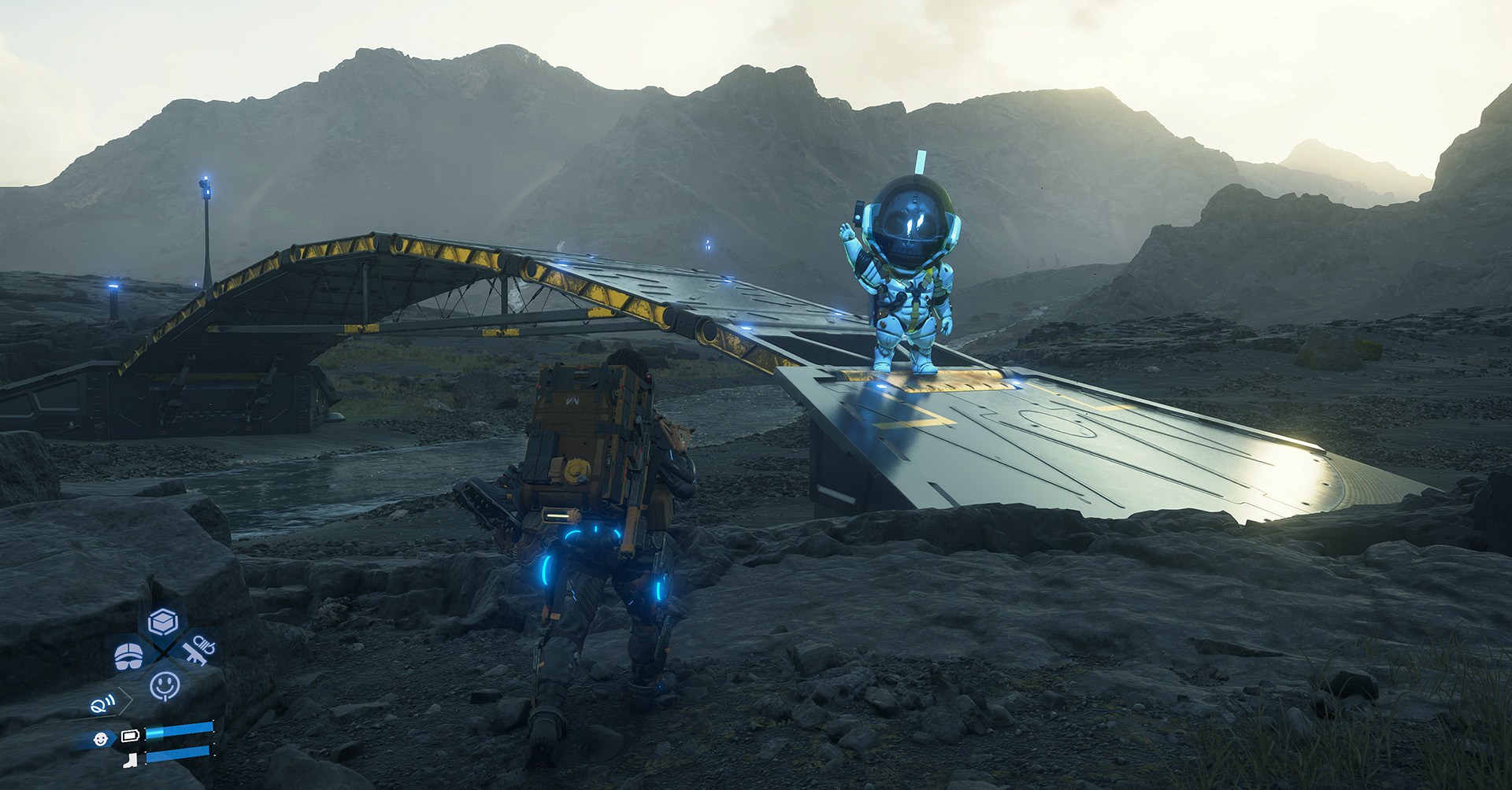 Sam se aproxima de uma ponte sobre um rio e uma figura robótica ondas da ponte em Death Stranding 2