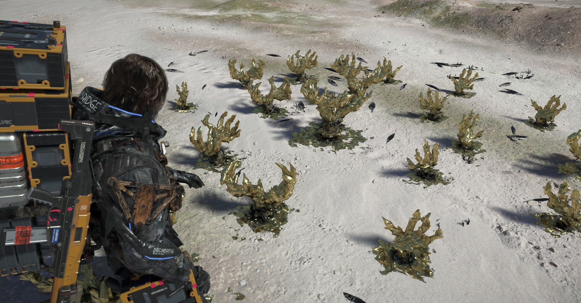 Uma captura de tela de 2 Stranding, mostrando o personagem olhando para cristais dourados que parecem garras. Uma captura de tela de 2 Stranding, mostrando o personagem olhando para cristais dourados que parecem garras.