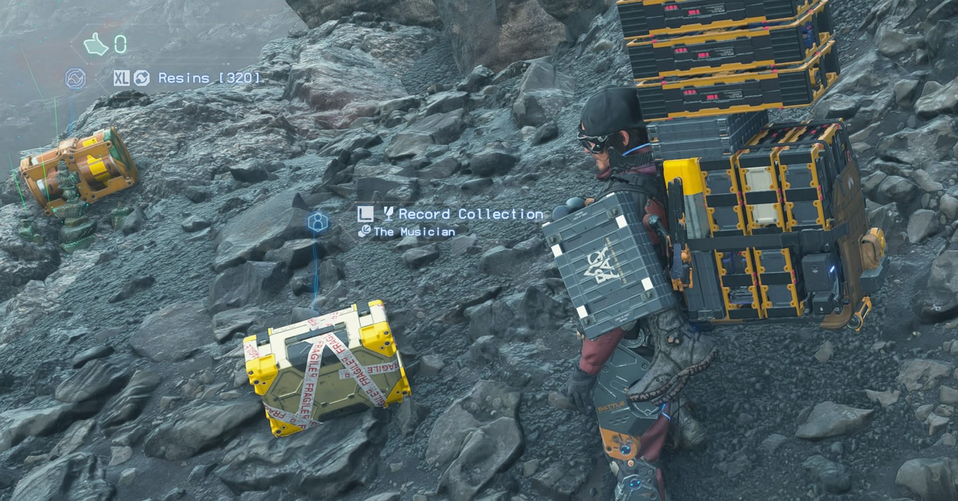 Uma captura de tela de 2 Stranding, mostrando o personagem principal Sam Porter em frente à caixa A indicou como  Uma captura de tela de 2 Stranding, mostrando o personagem principal Sam Porter em frente à caixa A indicou como