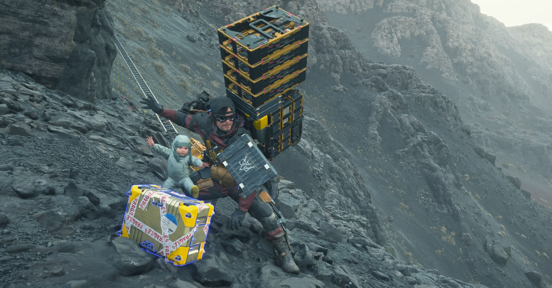 Uma captura de tela de 2 Stranding, mostrando Sam posando com um bebê com os braços abertos ao lado de uma caixa amarela brilhante. Uma captura de tela de 2 Stranding, mostrando Sam posando com um bebê com os braços abertos ao lado de uma caixa amarela brilhante.