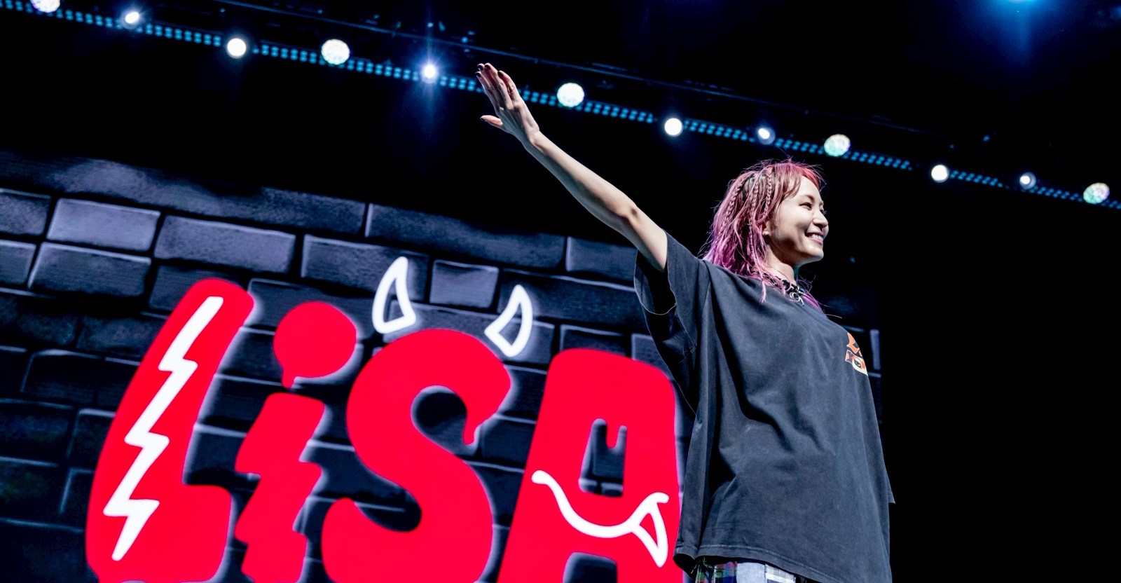 O músico do j-pop Lisa, no palco com uma enorme placa vermelha com o nome dela-com pequenos chifres de diabo no  O músico do j-pop Lisa, no palco com uma enorme placa vermelha com o nome dela-com pequenos chifres de diabo no