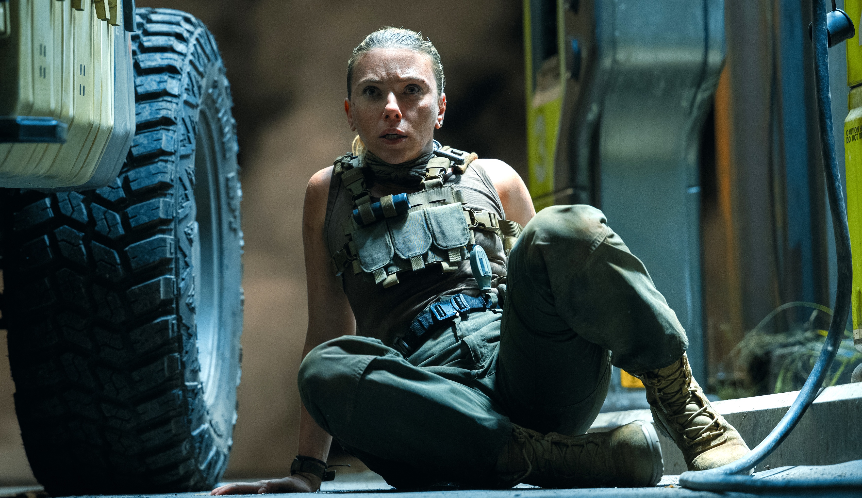 Zora (Scarlett Johansson), em equipamentos militares, fica no chão ao lado de um veículo gigante e parece enervoso em algo que se aproxima da tela em Jurassic Park: Rebirth