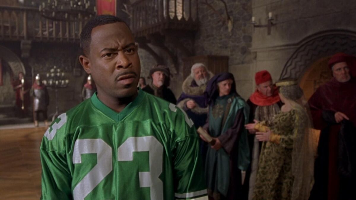 Uma captura de tela de um homem em uma camisa de futebol entre as pessoas vestidas com guarda -roupa medieval. Martin Lawrence em Black Knight 2001