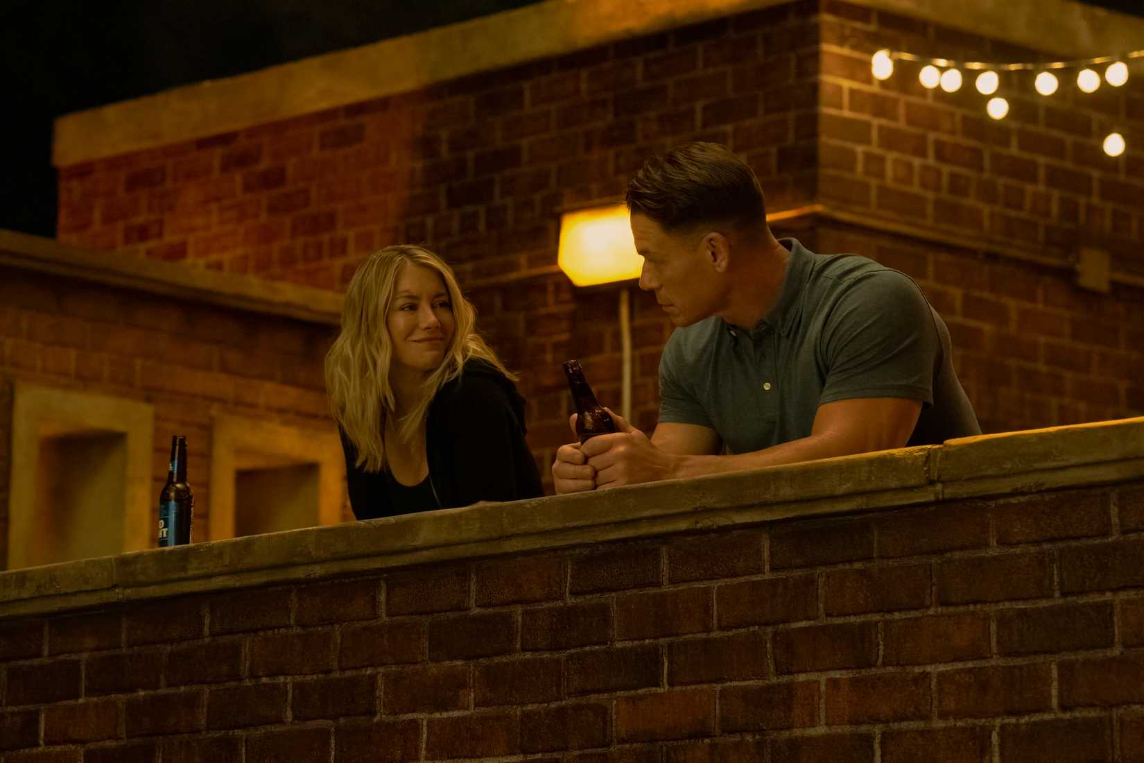 Harcourt (Jennifer Holland) e Peacemaker (John Cena) compartilham um momento de silêncio juntos em um telhado na segunda temporada, episódio 1 de Peacemaker