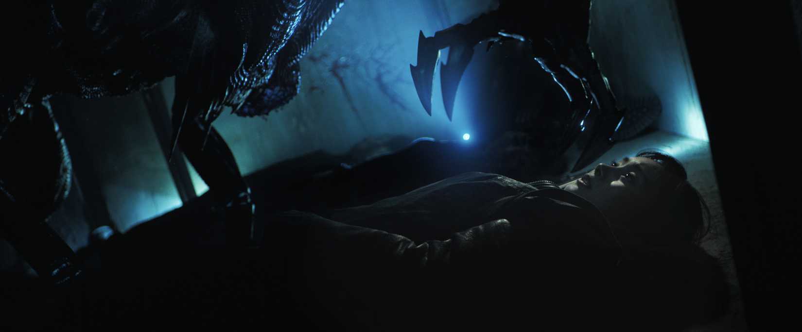 Uma criatura alienígena se inclina sobre uma mulher aterrorizada com uma garra estendida