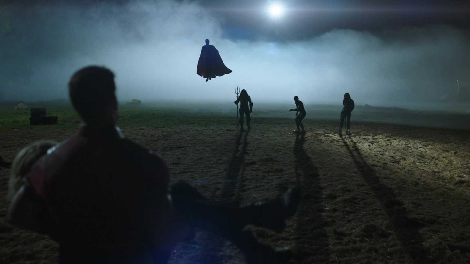 Paacemaker (John Cena), visto por trás enquanto carrega um companheiro de equipe inconsciente para longe de uma batalha, se aproxima das figuras silhuetas de Superman, Aquaman, Flash e Mulher Maravilha na primeira temporada, episódio 8