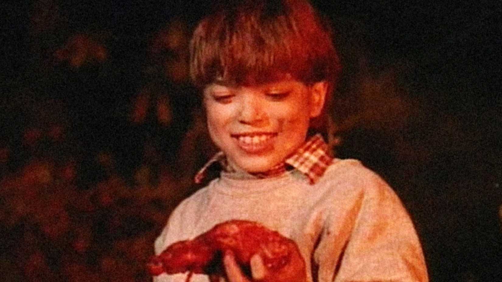 Uma criança sorridente e manchada de sangue mantém um órgão humano sangrento em cuidado! Crianças em brincadeira