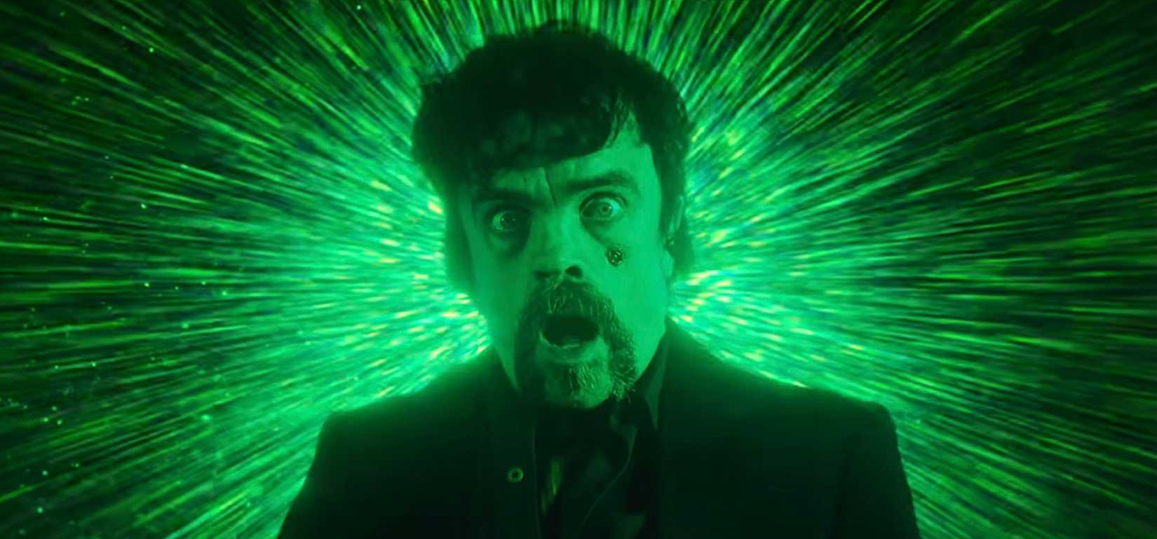 Peter Dinklage no vingador tóxico, gritando e horrorizado com uma explosão de luz verde atrás dele
