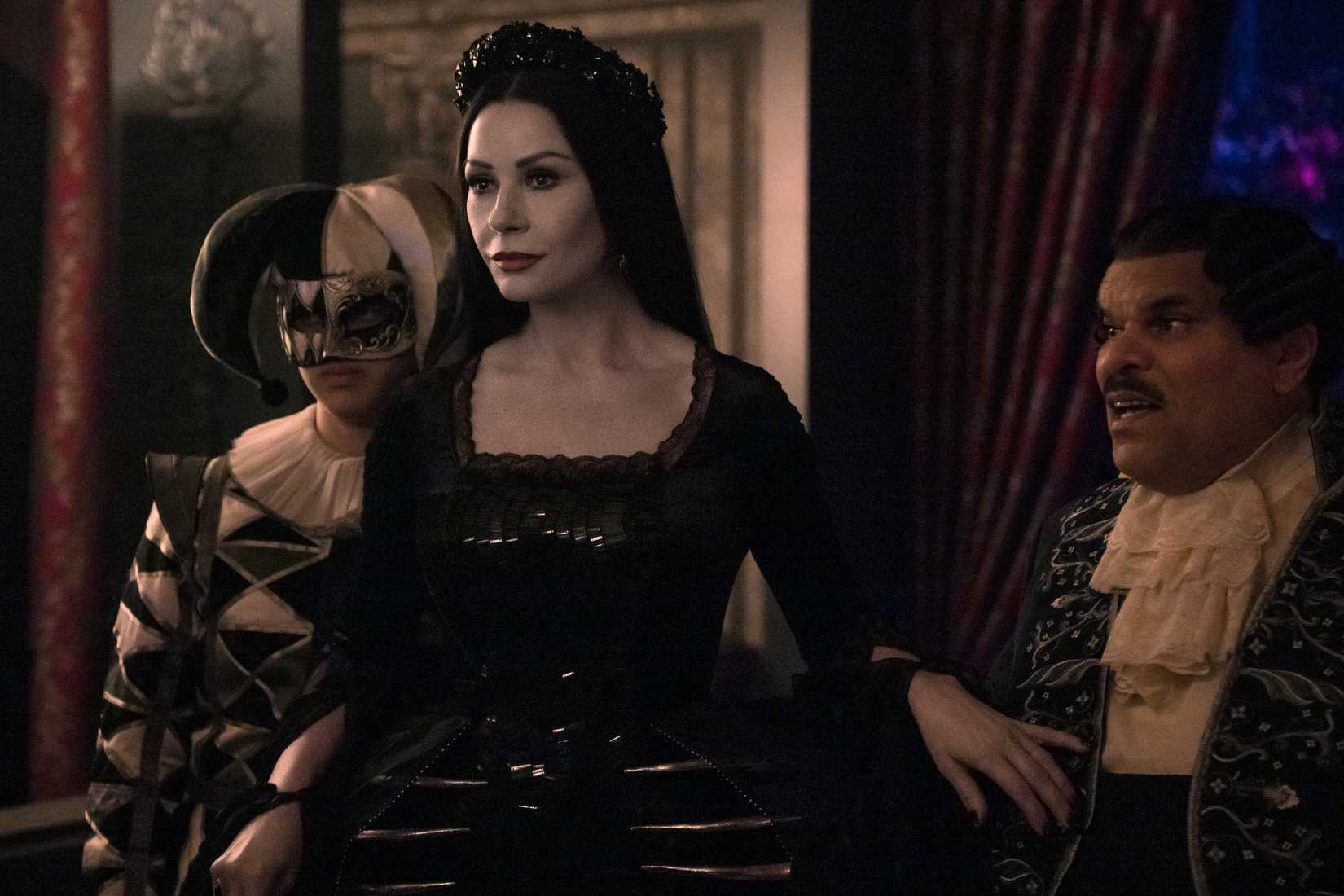 Imagem da quarta -feira da Netflix. A Morticia fica em frente a Gomez e Pugsley, uma mão protetora sobre o Cravat de Gomez.