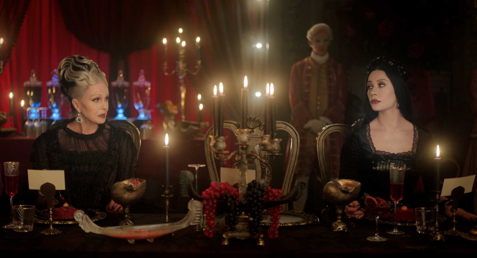 Imagem de quarta -feira com Hester e sua filha, Morticia. Eles olham um para o outro através de uma mesa de jantar.