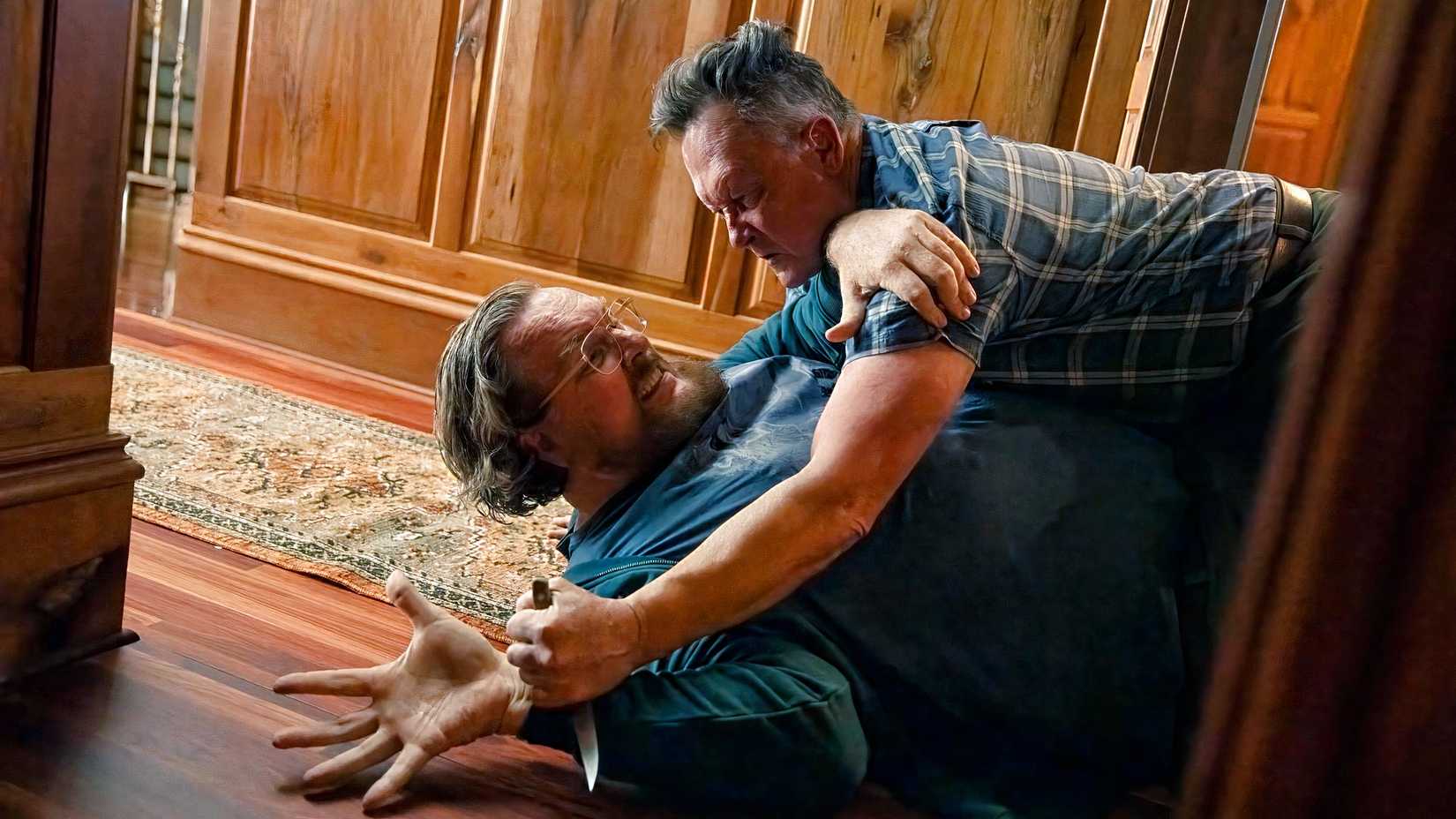 John Economos (Steve Agee) está preso ao chão por Auggie Smith (Robert Patrick) em pacificador