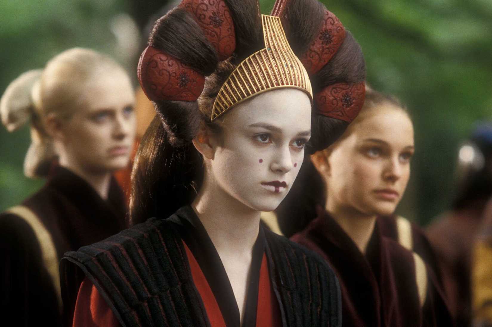 Uma imagem de Sabe (Keira Knightley) de Star Wars: Phantom Menace. Ela usa maquiagem branca e um capacete tradicional.