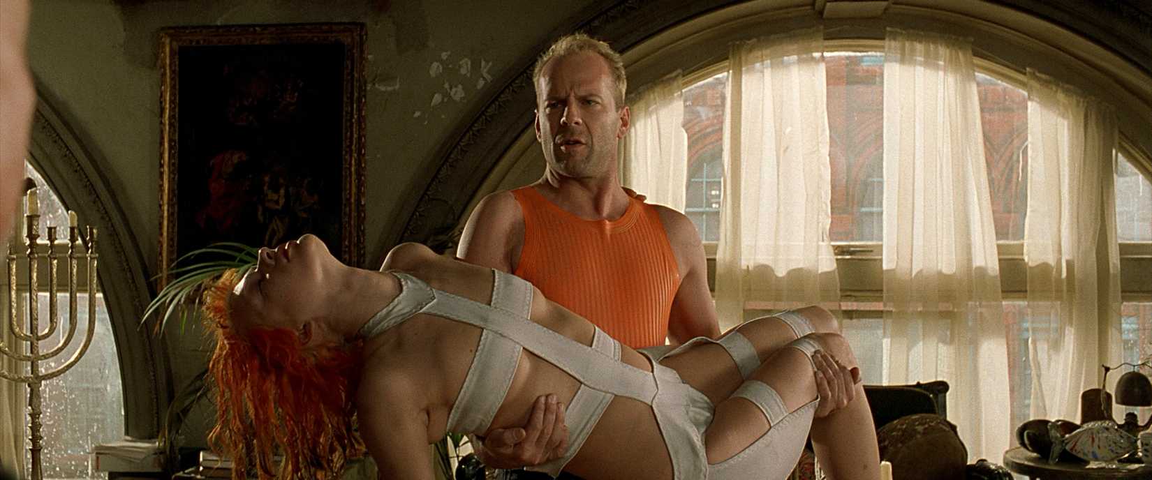 Bruce Willis em um top laranja sem mangas mantém Milla Jovovich em um vestido curativo no quinto elemento