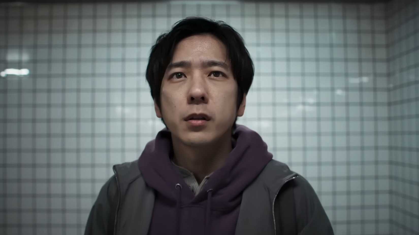Uma captura de tela do trailer de saída 8 mostrando o protagonista, um japonês usando um capuz