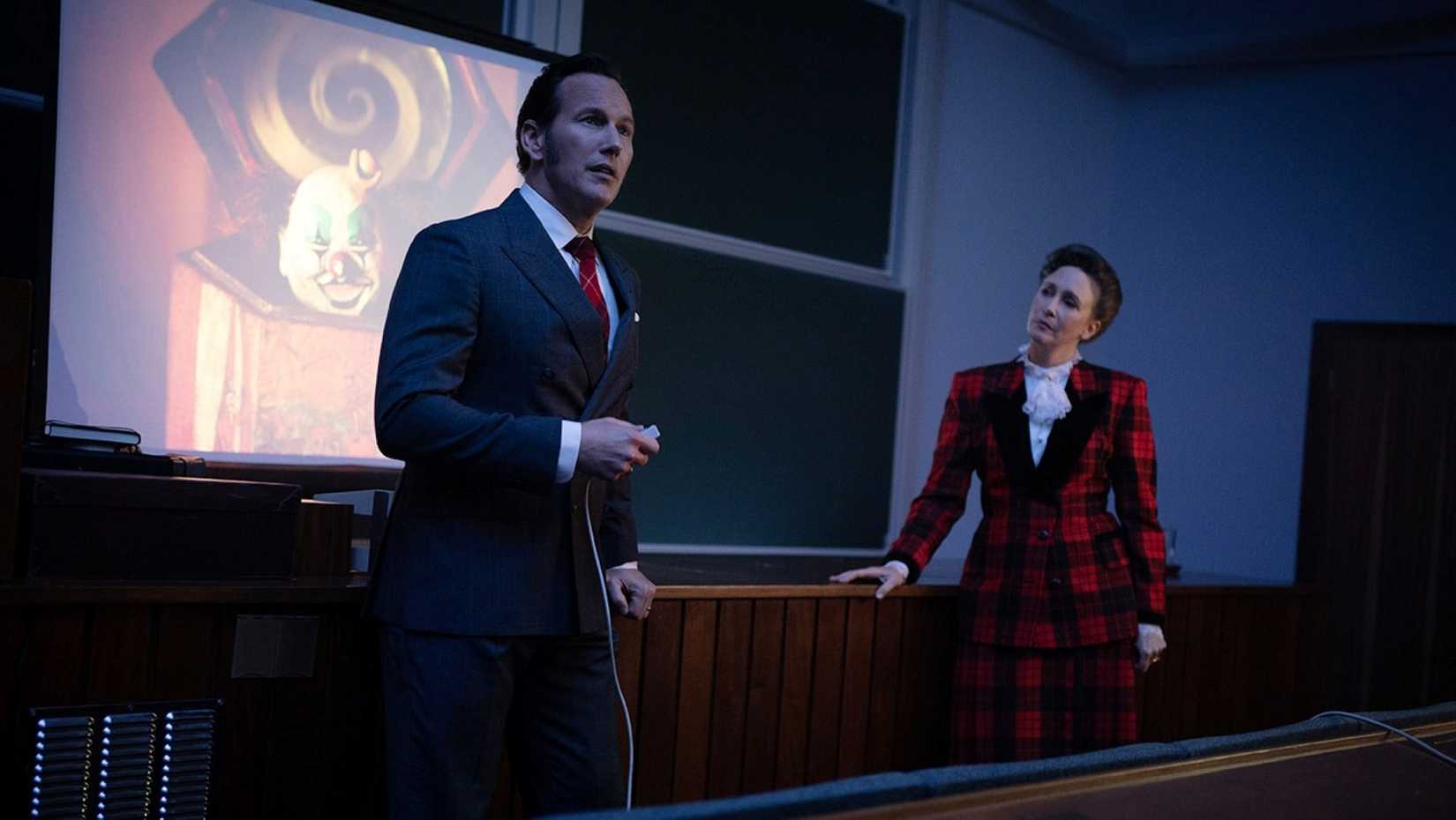 Ed e Lorraine Warren, interpretados por Patrick Wilson e Vera Farmiga, Palestra uma sala de aula sobre ocorrências paranormais em uma cena de The Conjuring: Last Rites 