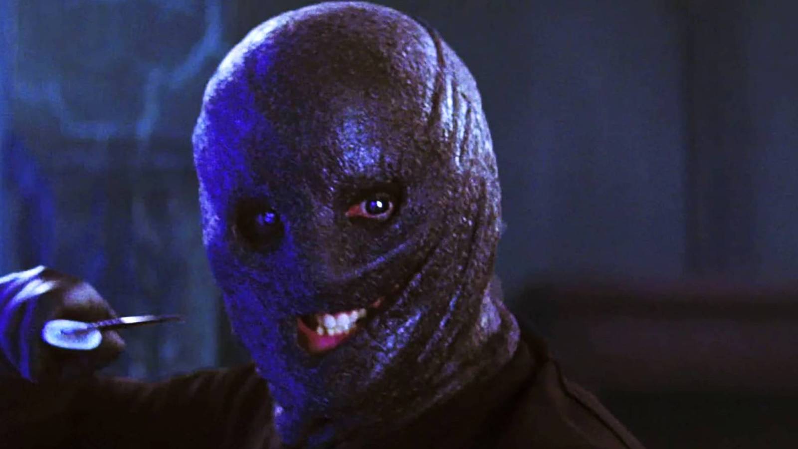 Um homem sorridente em um capuz de aparência gordurosa e de aparência oleosa segura um objeto nítido no filme de 2009 The Collector