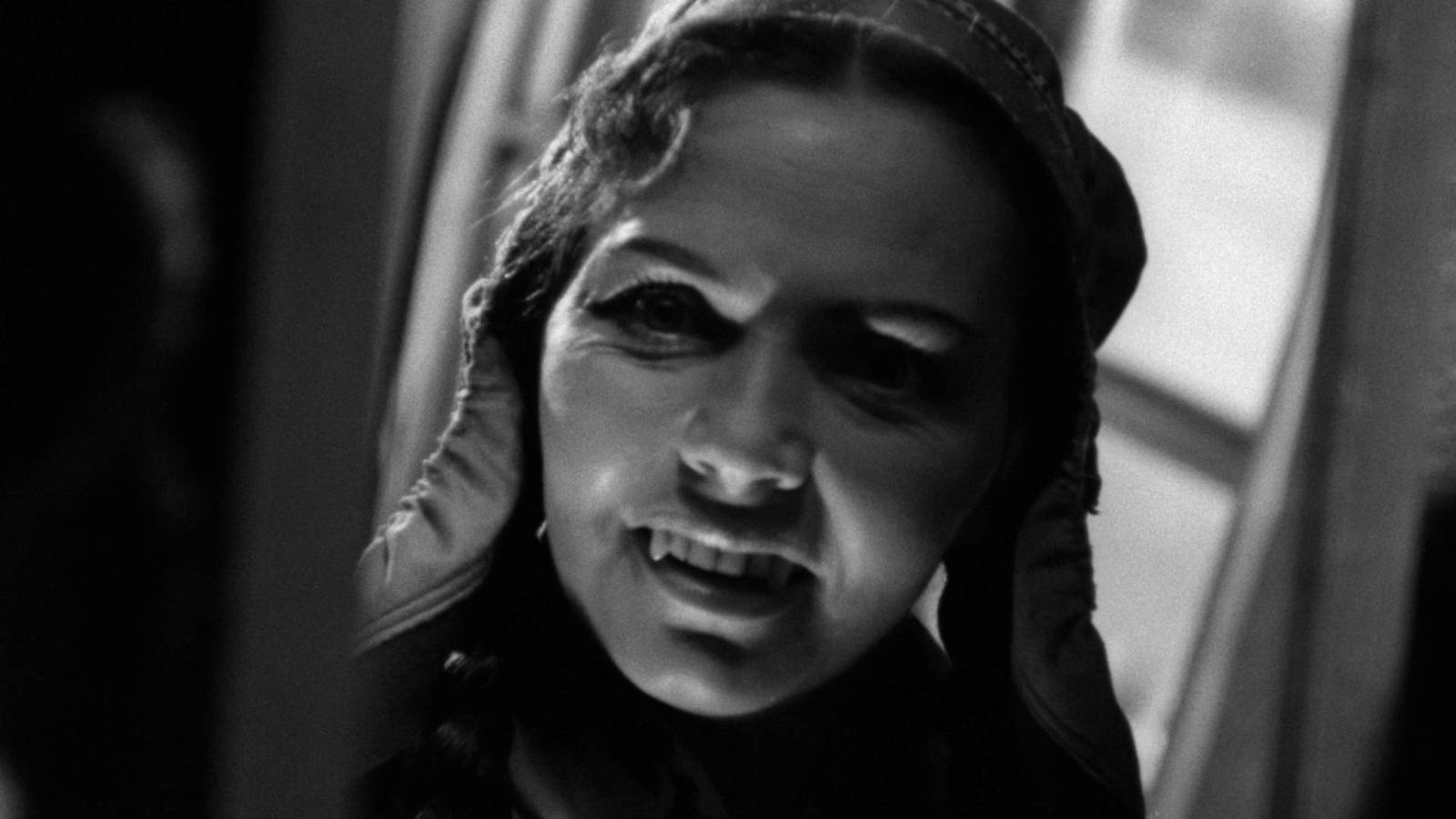 Uma imagem em preto e branco de uma mulher vestindo um chapéu finlandês tradicional e dentes de vampiro esportivo na rena branca