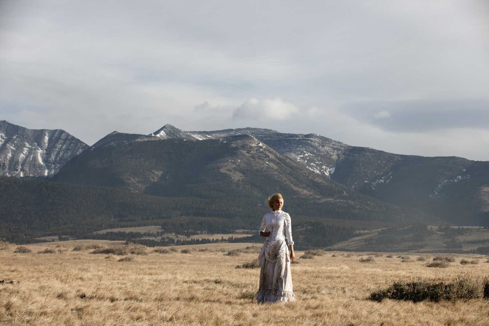 Elsa (Isabel May) em um campo vazio com montanhas ao fundo em 1883