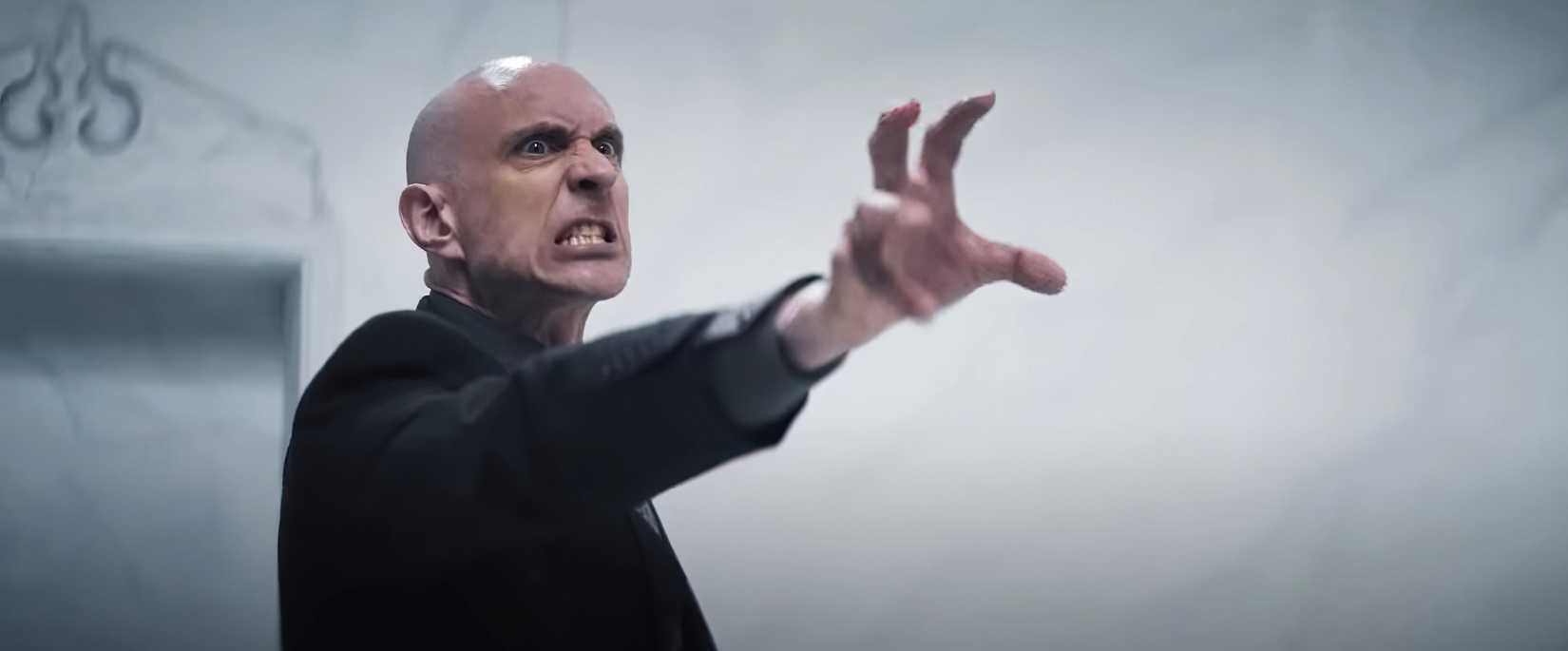 Um homem careca e rosnante (Charles Hubbell) estende a mão em forma de garra em The Harbinger