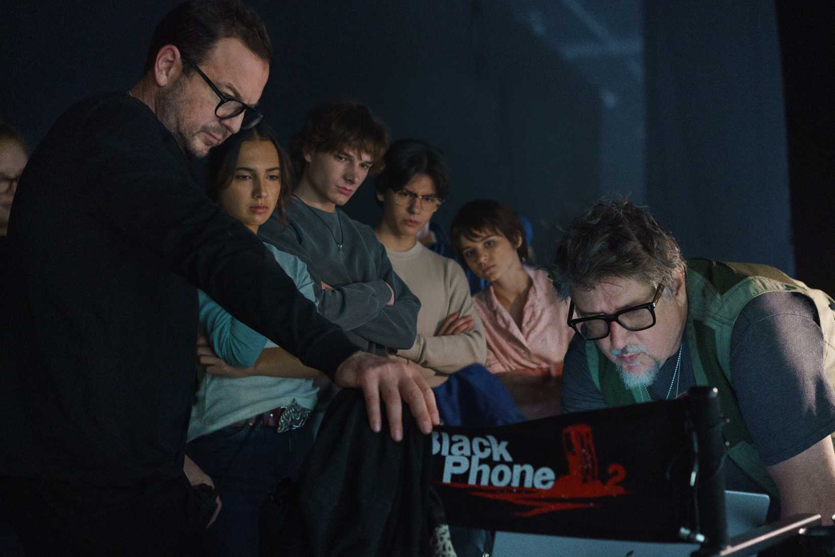 O produtor executivo Jason Blumenfeld, os atores Arianna Rivas, Mason Thames, Miguel Mora e Madeleine McGraw e o diretor Scott Derrickson se reúnem em torno de um laptop no set de Black Phone 2