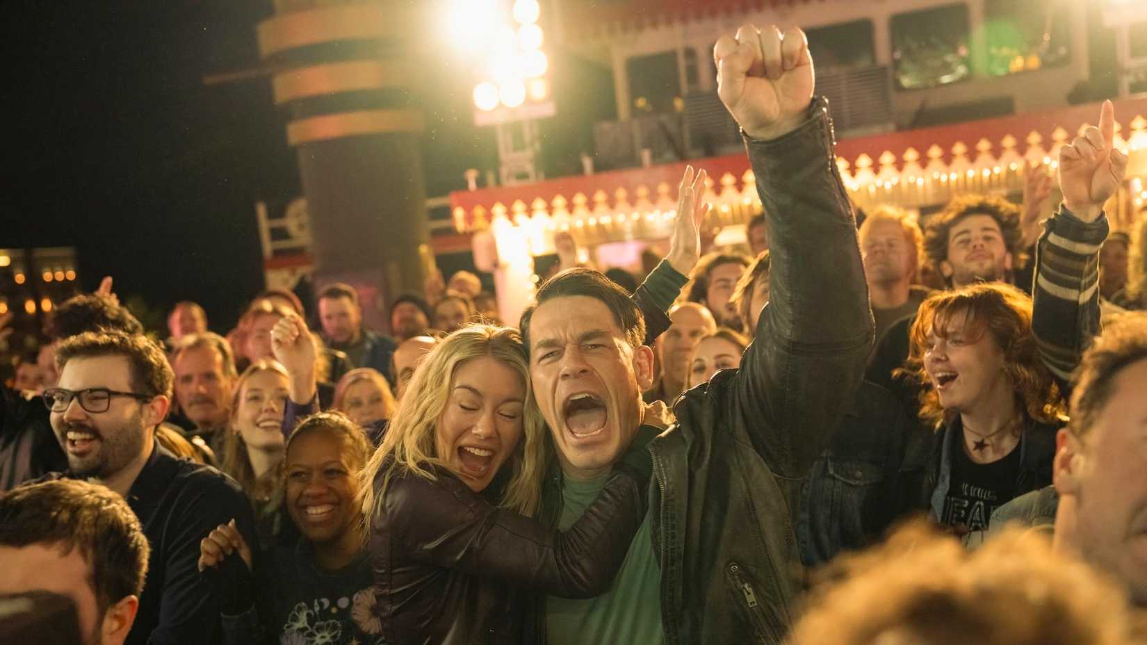 Emilia Harcourt (Jennifer Holland) abraça Chris Smith (John Cena) que comemora durante show em um barco em Peacemaker