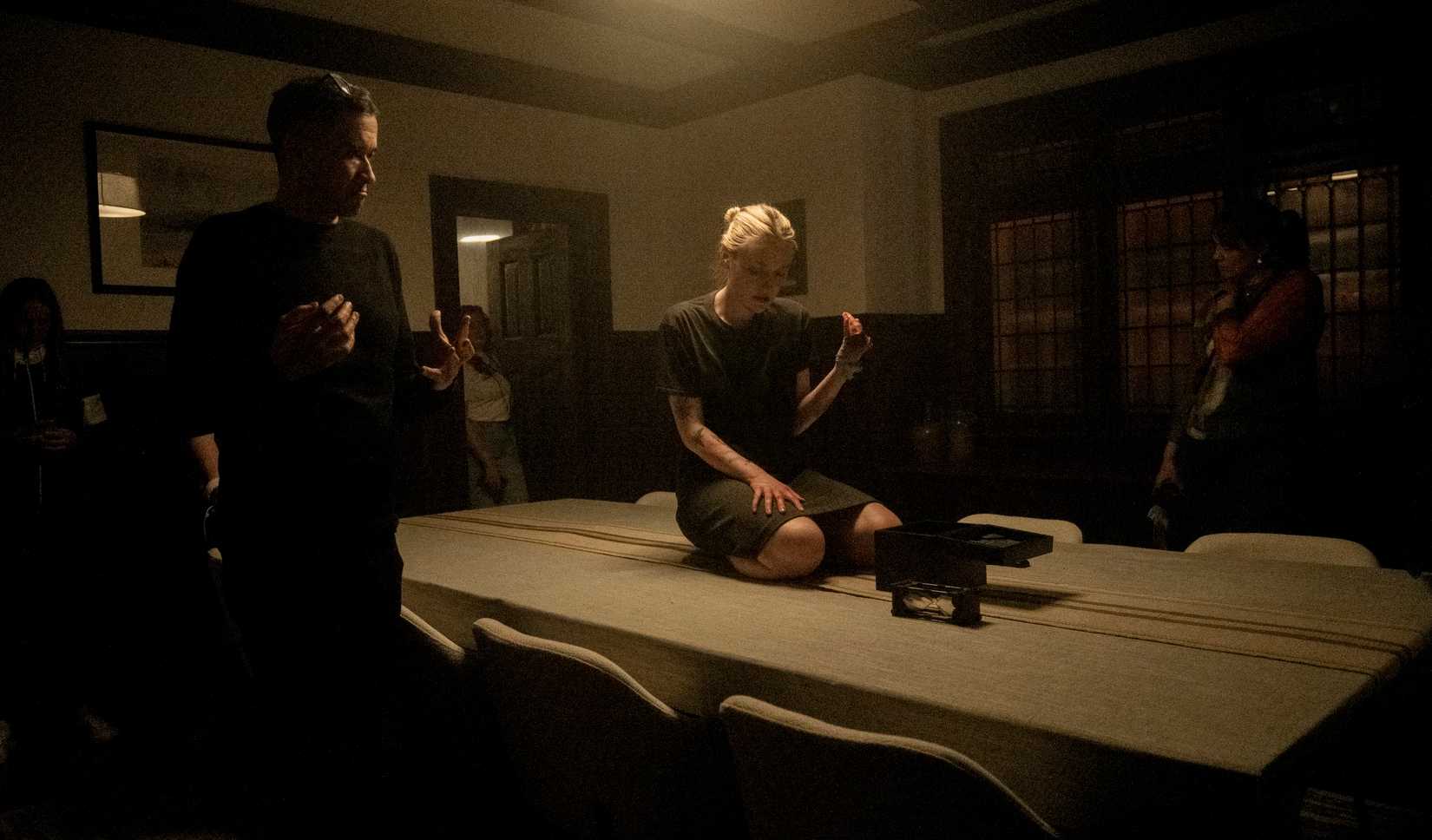 O diretor Bryan Bertino observa as câmeras enquanto Dakota Fanning se ajoelha na mesa da cozinha no set de Vicious