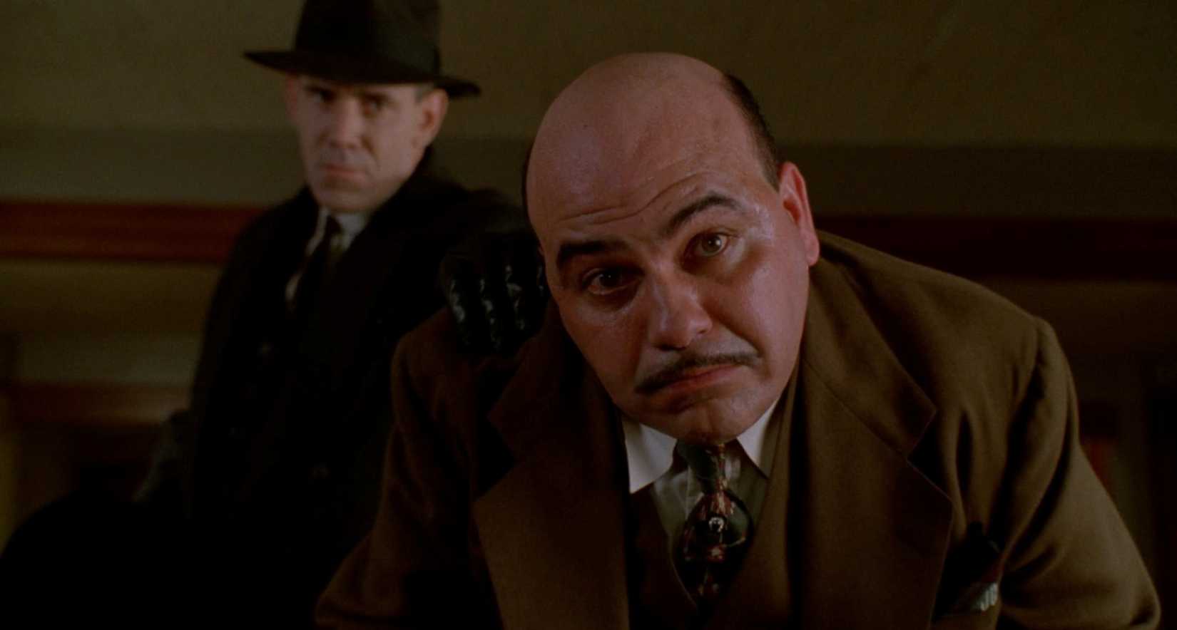 Jon Polito faz uma careta de frustração como um gângster de temperamento curto em uma cena de Miller's Crossing