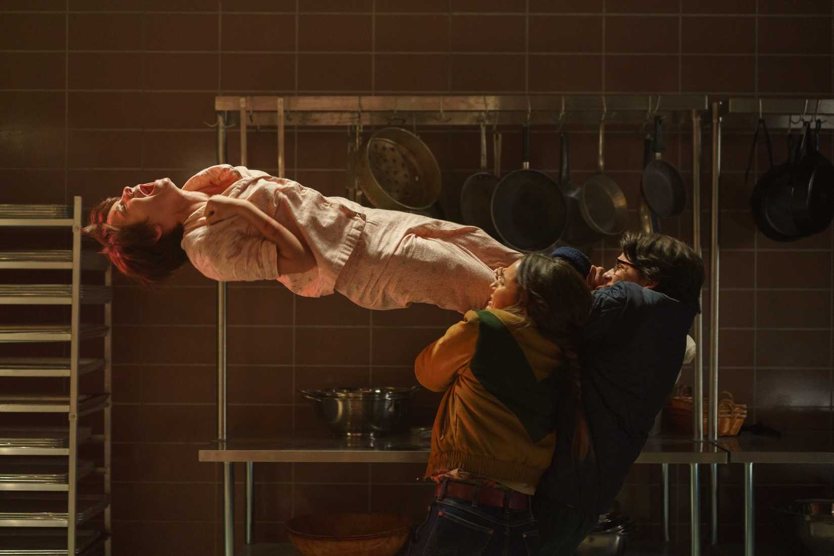 Gwen (Madeleine McGraw), de pijama rosa, flutua de costas no ar, gritando e apertando a garganta, enquanto várias pessoas se agarram às suas pernas e tentam puxá-la para baixo em Black Phone 2