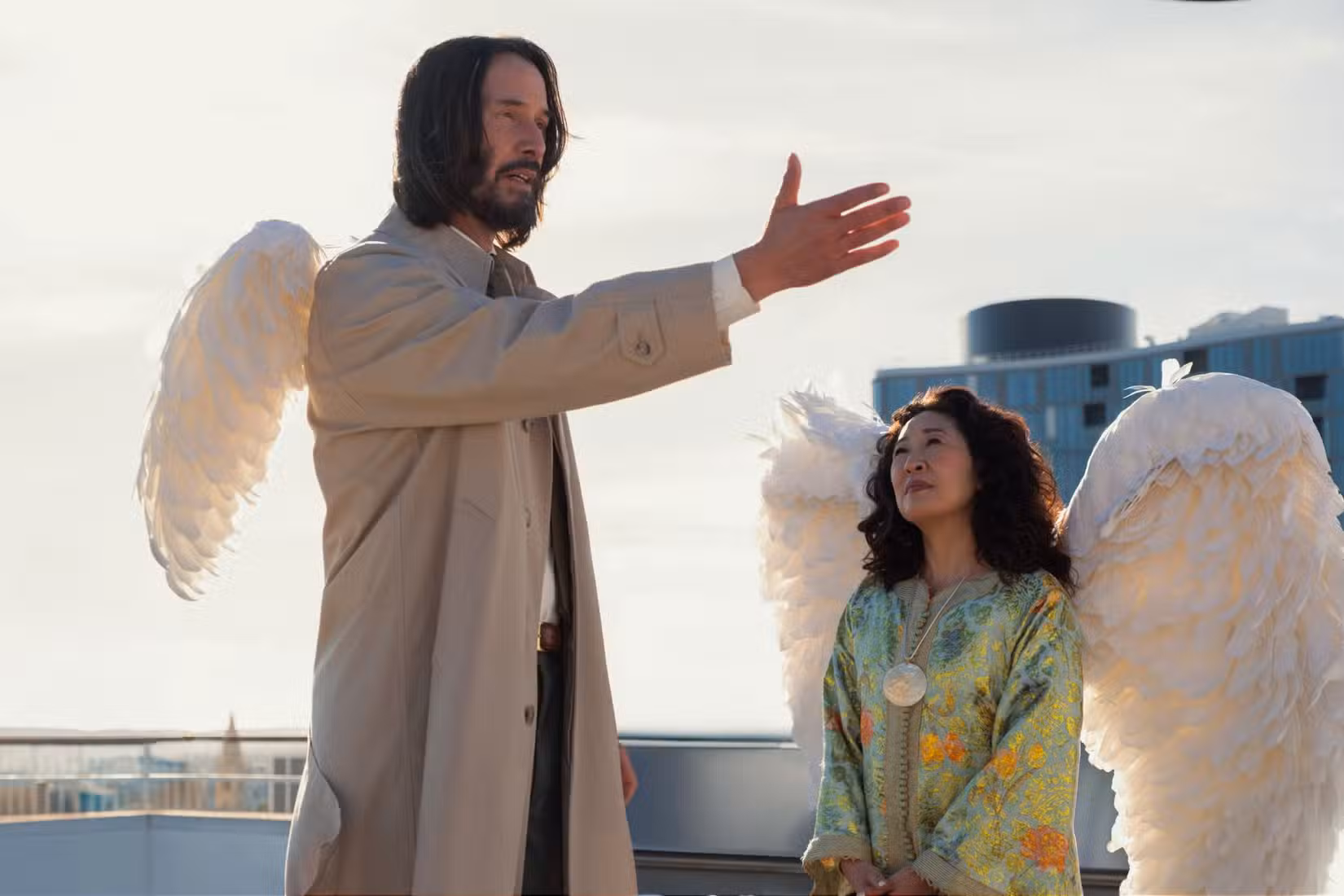 Keanu Reeves como Gabriel, um anjo da guarda com asas embaraçosamente pequenas, estende a mão em um gesto dramático enquanto seu chefe, um anjo interpretado por Sandra Oh, observa pacientemente