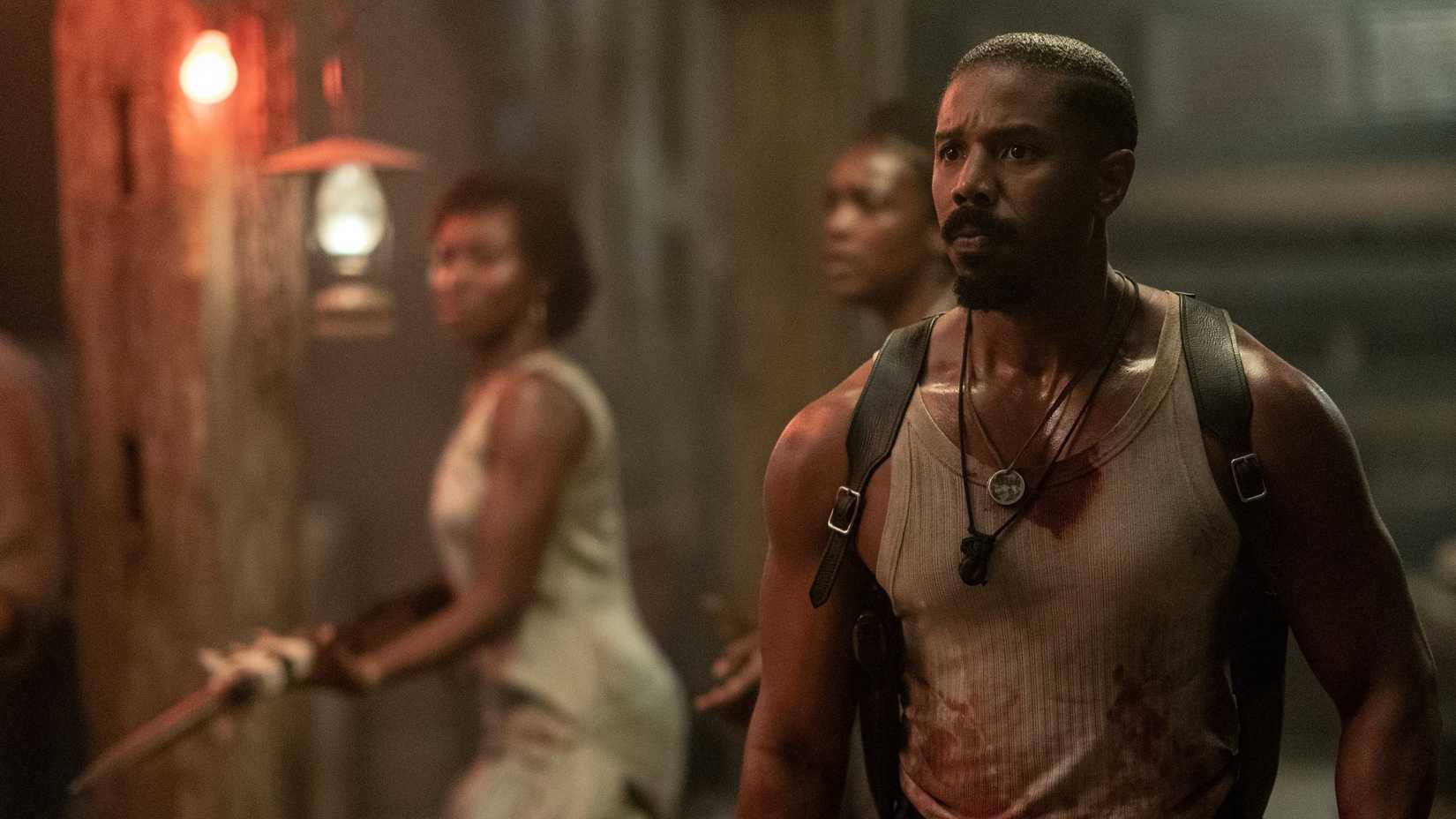 Michael B. Jordan, suado e com uma camiseta sem mangas manchada de sangue, parece preocupado e abatido em Sinners, de Ryan Coogler