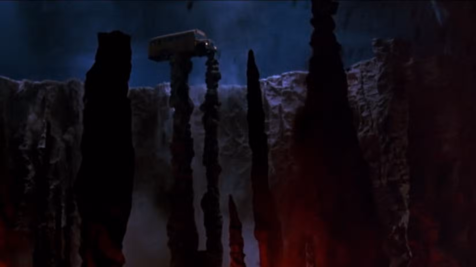 Um ônibus balançando na beira de dois pilares de pedra sobre o que parecem ser as profundezas do inferno de A Nightmare on Elm Street 2: Freddy's Revenge