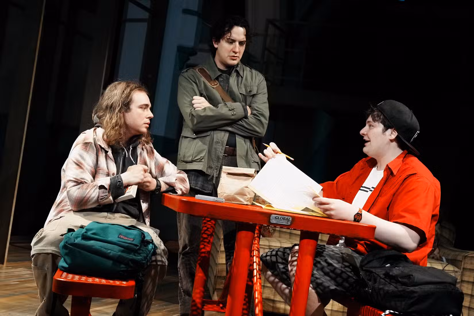 Três personagens adolescentes da peça Iniciativa reuniram-se em torno de uma mesa jogando Dungeons & Dragons.