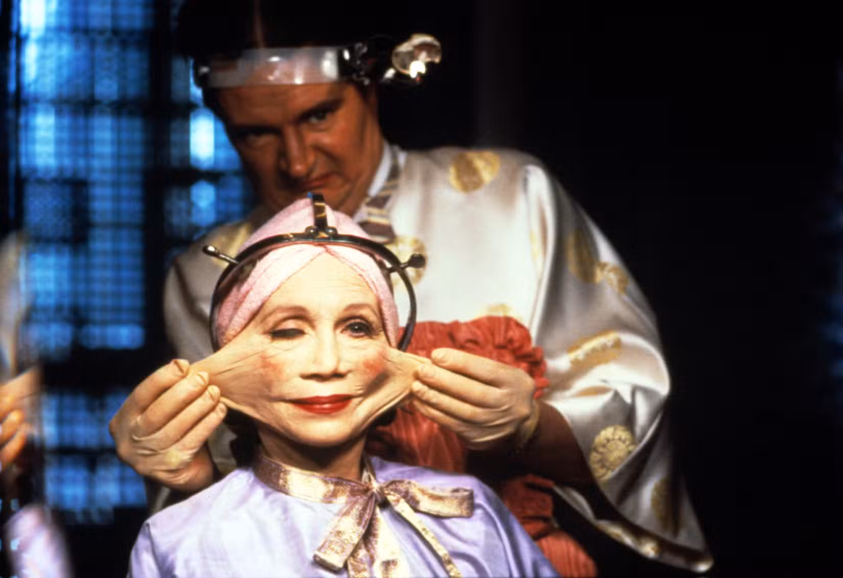 Uma imagem do filme de Terry Gilliam de 1985, Brasil. Retrata Katherine Helmond como a Sra. Ida Lowry com o rosto esticado desconfortavelmente.