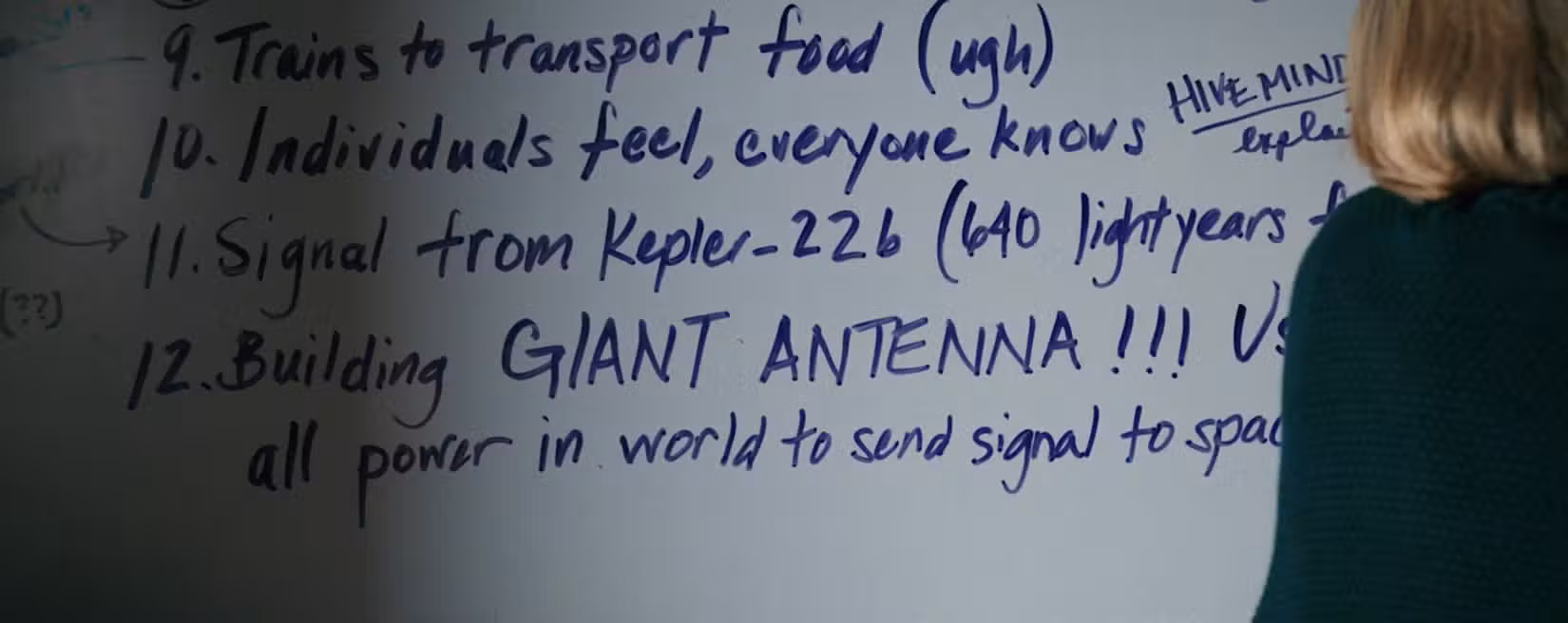 Carol (Rhea Seehorn) fica de costas para a câmera, diante de um quadro branco coberto de fatos sobre os Outros. Proeminentemente no meio, em letras maiúsculas, estão as palavras "ANTENA GIGANTE!!!"
