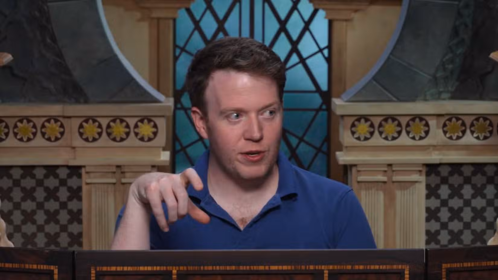Uma captura de tela do episódio 8 do Cooldown para Critical Role Campaign 4. Apresenta Brennan Lee Mulligan, vestindo uma camisa azul, gesticulando com as mãos atrás de uma manga de Dungeons and Dragon's DM. 