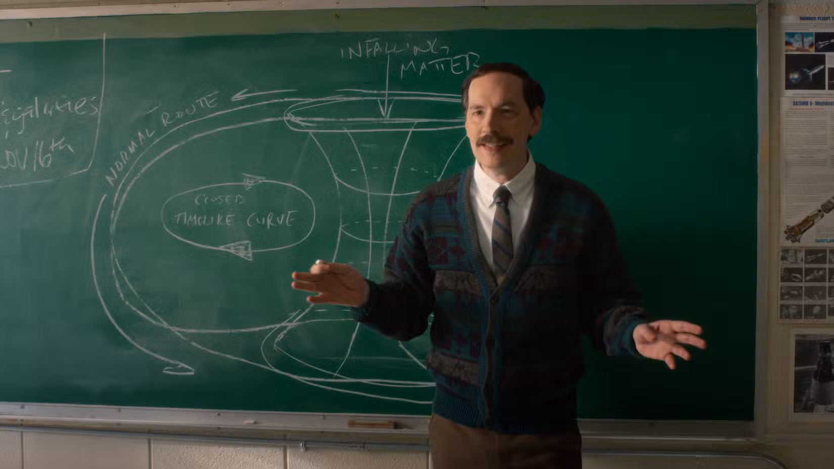 O professor de ciências da Hawkins Middle School, Sr. Clarke (Randy Havens), dá uma lição sobre buracos de minhoca em frente a um quadro-negro verde na 5ª temporada de Stranger Things