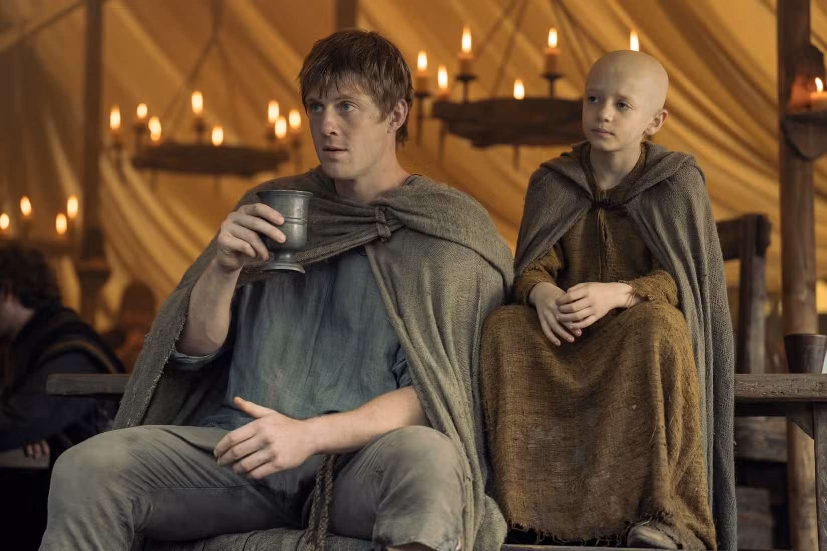 Dunk (Peter Claffey) e Egg (Dexter Sol Ansell), um homem alto e um menino careca, sentam-se juntos na prequela de Game of Thrones, Um Cavaleiro dos Sete Reinos 