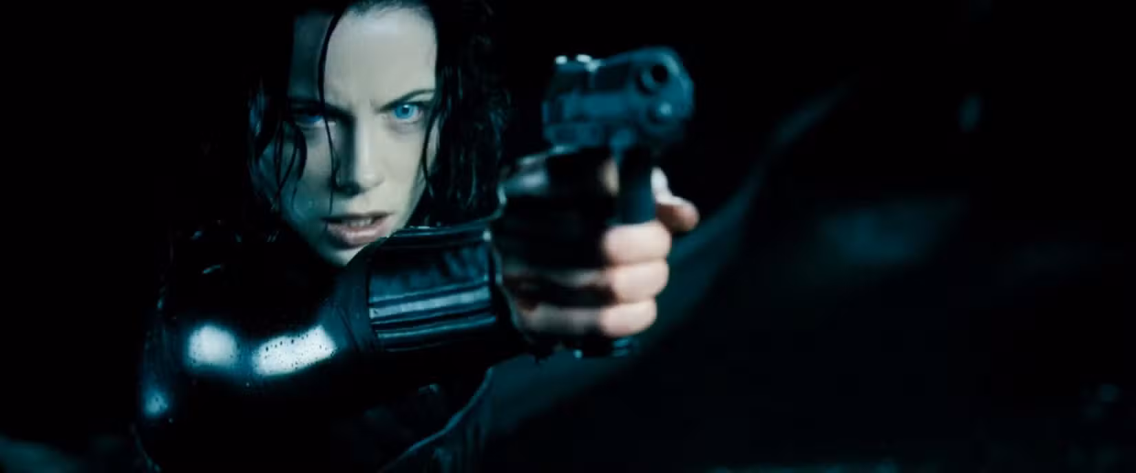 Selene (Kate Beckinsale) aponta sua pistola personalizada para alguém fora da tela enquanto parece irritada em uma cena de Underworld: Evolution