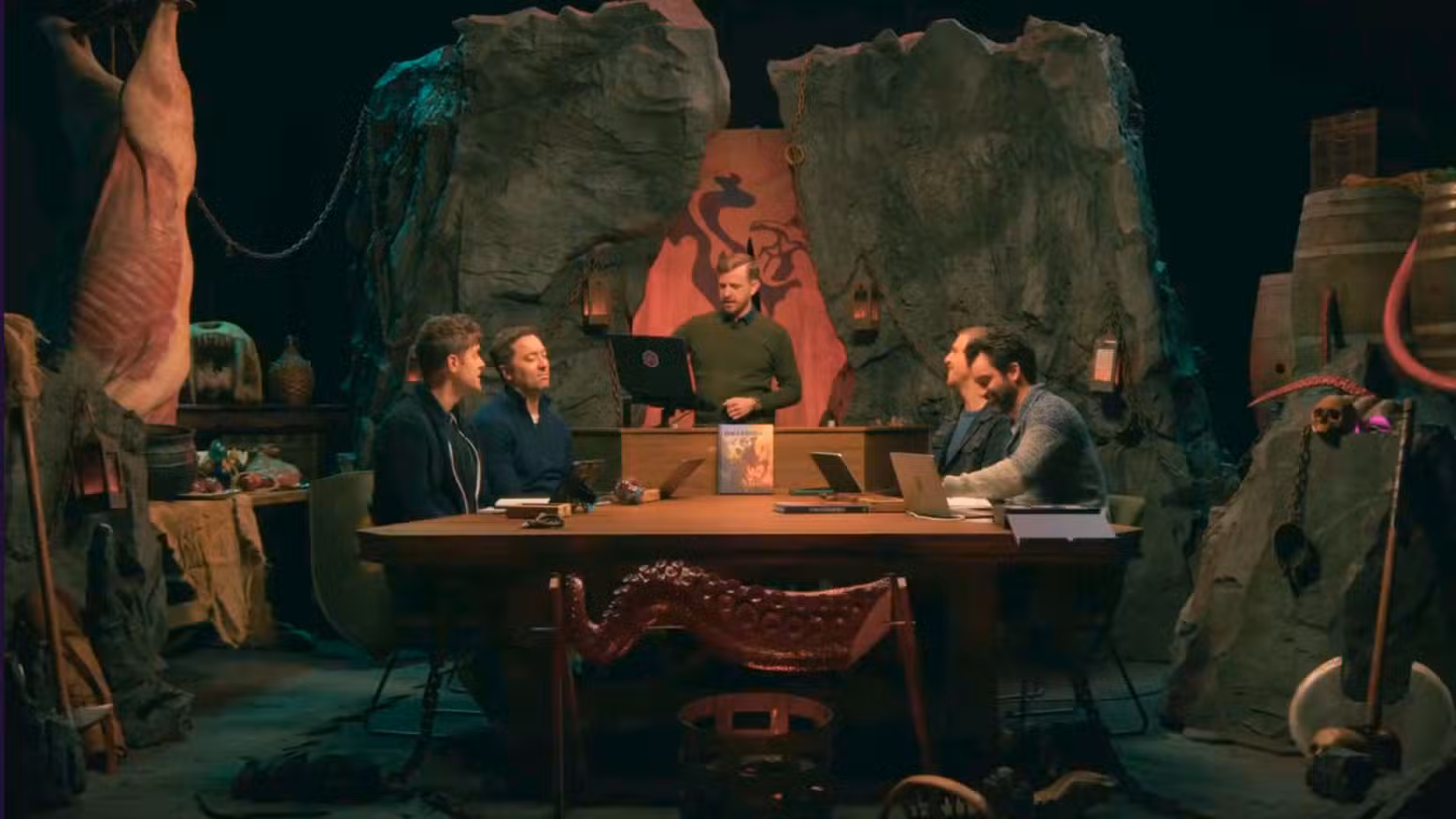 Uma imagem do trailer de Daggerheart: Azerim. Mostra cinco homens sentados a uma longa mesa, rodeados por imagens fantasiosas.