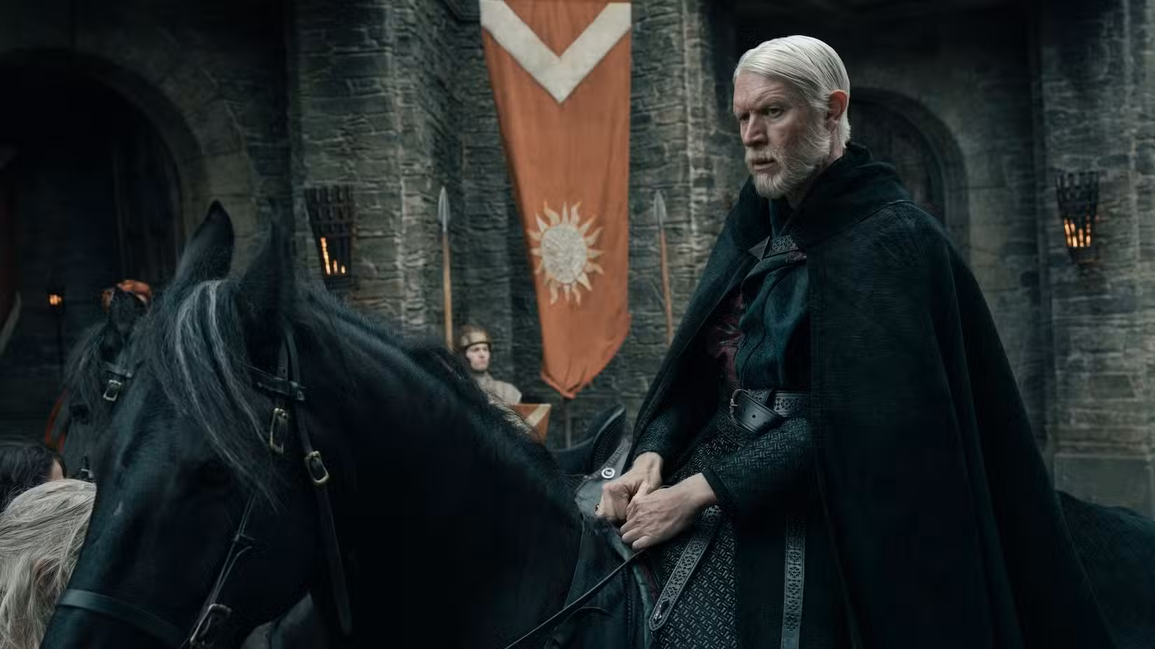 Maekar Targaryen (Sam Spruell) está todo vestido de preto sentado em cima de um cavalo preto em frente a um castelo em O Cavaleiro dos Sete Reinos