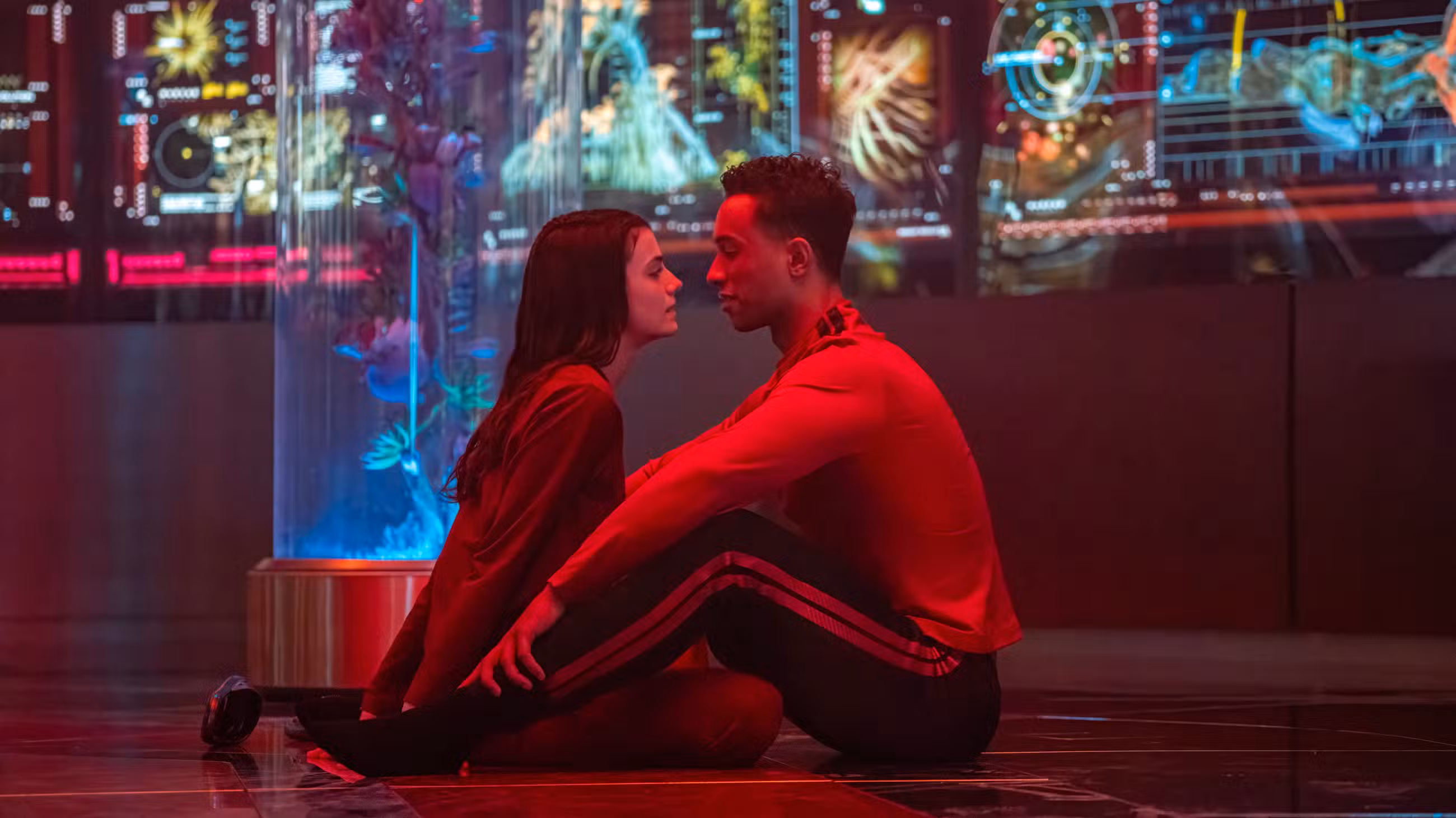Caleb Mir (Sandro Rosta) e Tarima Sadal (Zoë Steiner) se inclinam para um beijo enquanto estão sentados no chão de uma sala cheia de telas na Academia da Frota Estelar