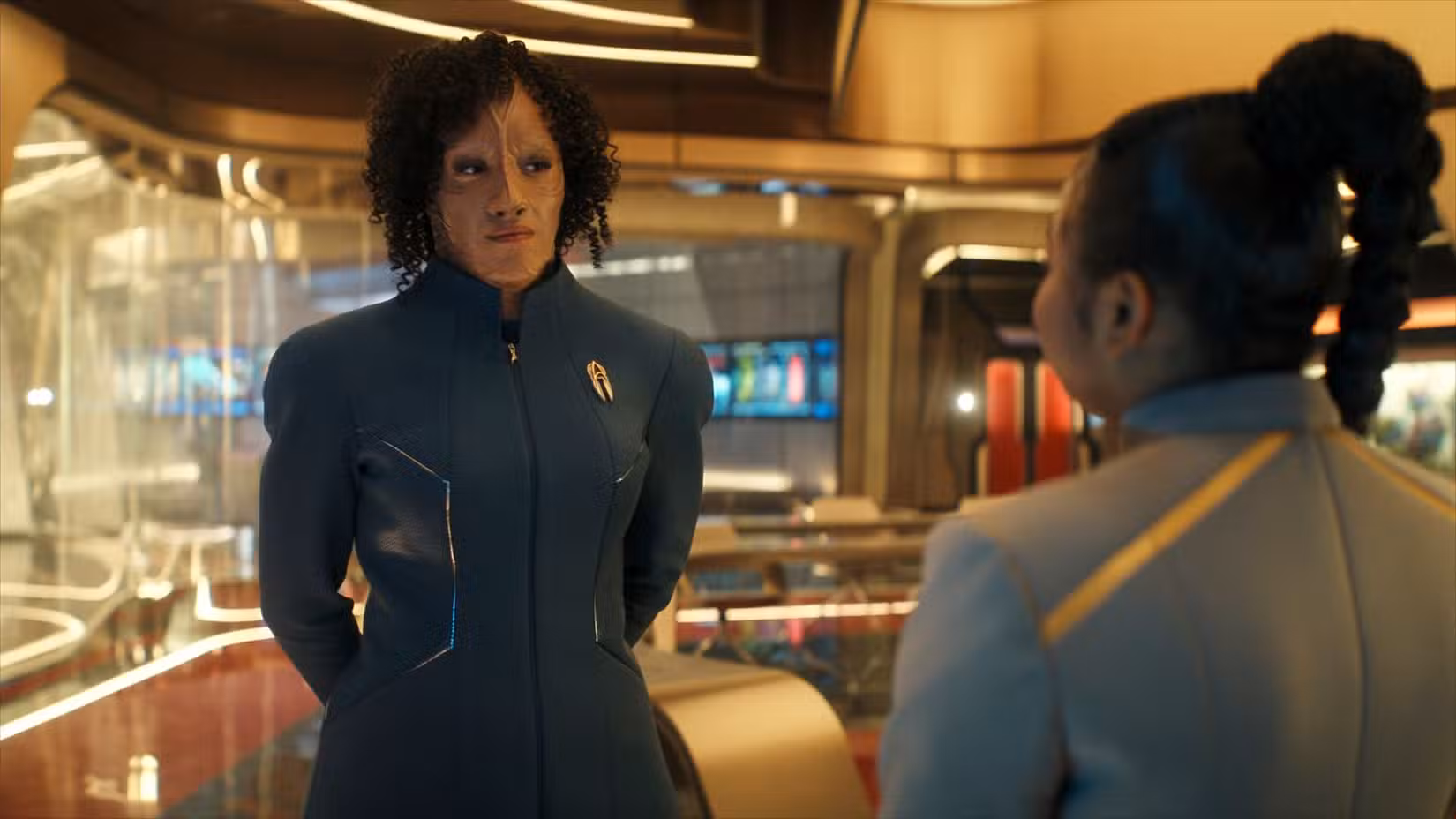 Illa Dax (Tawny Newsome), uma cardassiana de uniforme azul, está em uma sala de aula conversando com Sam (Kerrice Brooks), um estudante de uniforme cinza