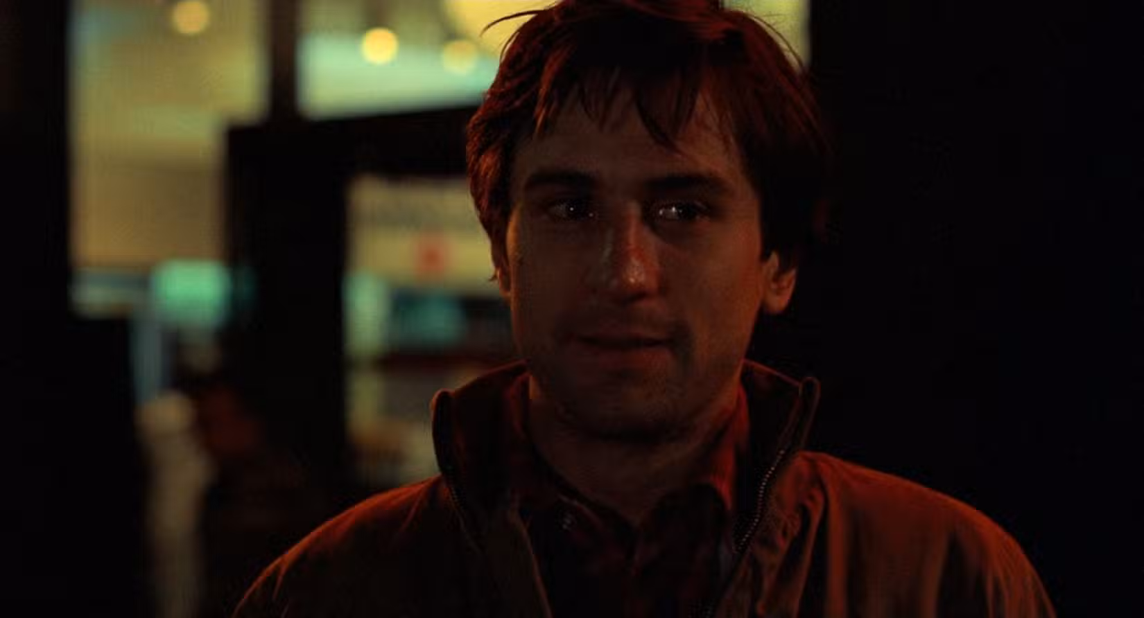 Um close-up médio de Travis Bickle (Robert De Niro) parado nas ruas de Nova York, banhado por luz neon vermelha.