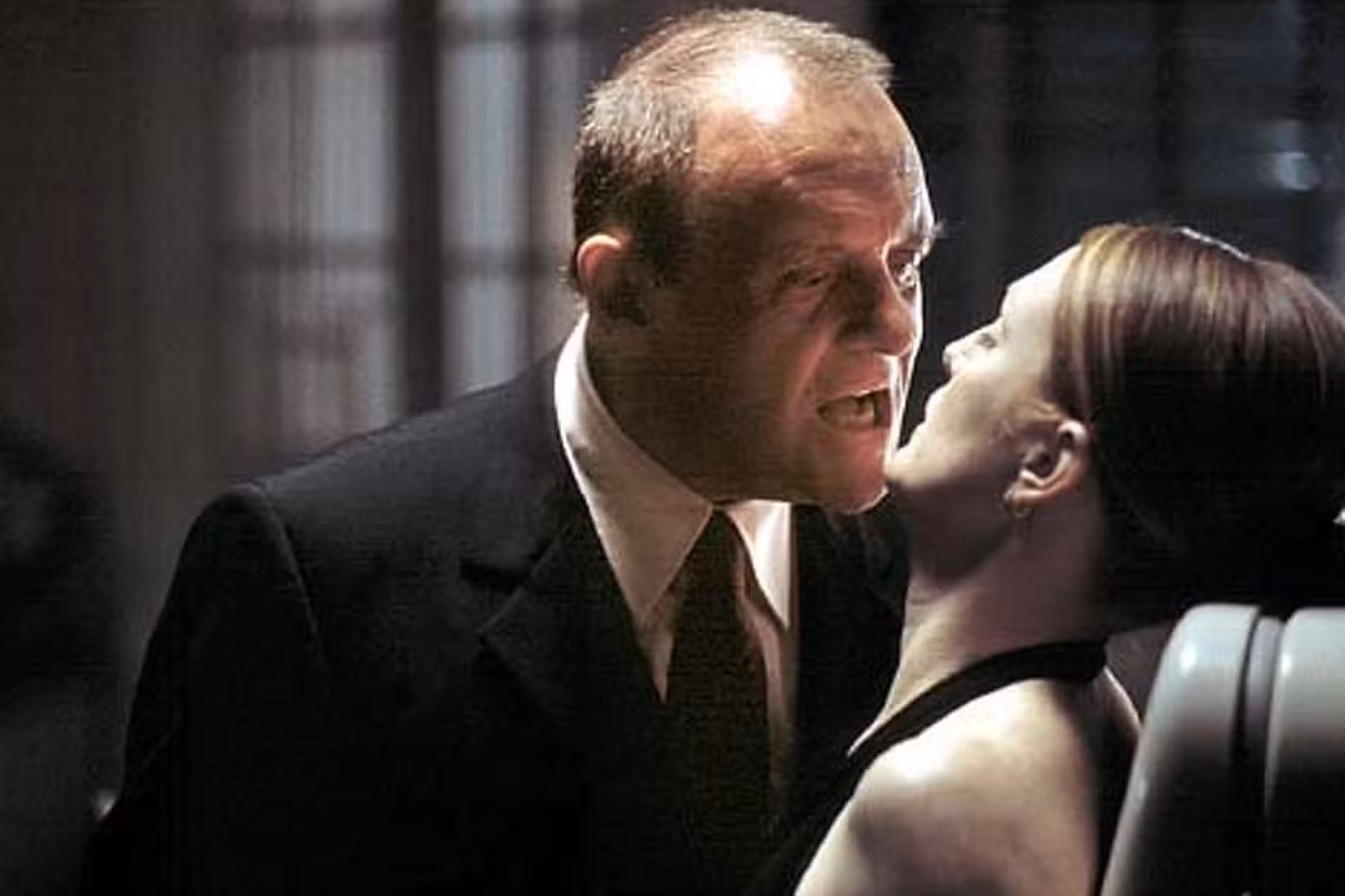 Hannibal Lecter (Anthony Hopkins) se inclina ameaçadoramente para falar com Clarice (Julianne Moore) presa, suas bocas desconfortavelmente fechadas, em uma cena de Hannibal (2001)