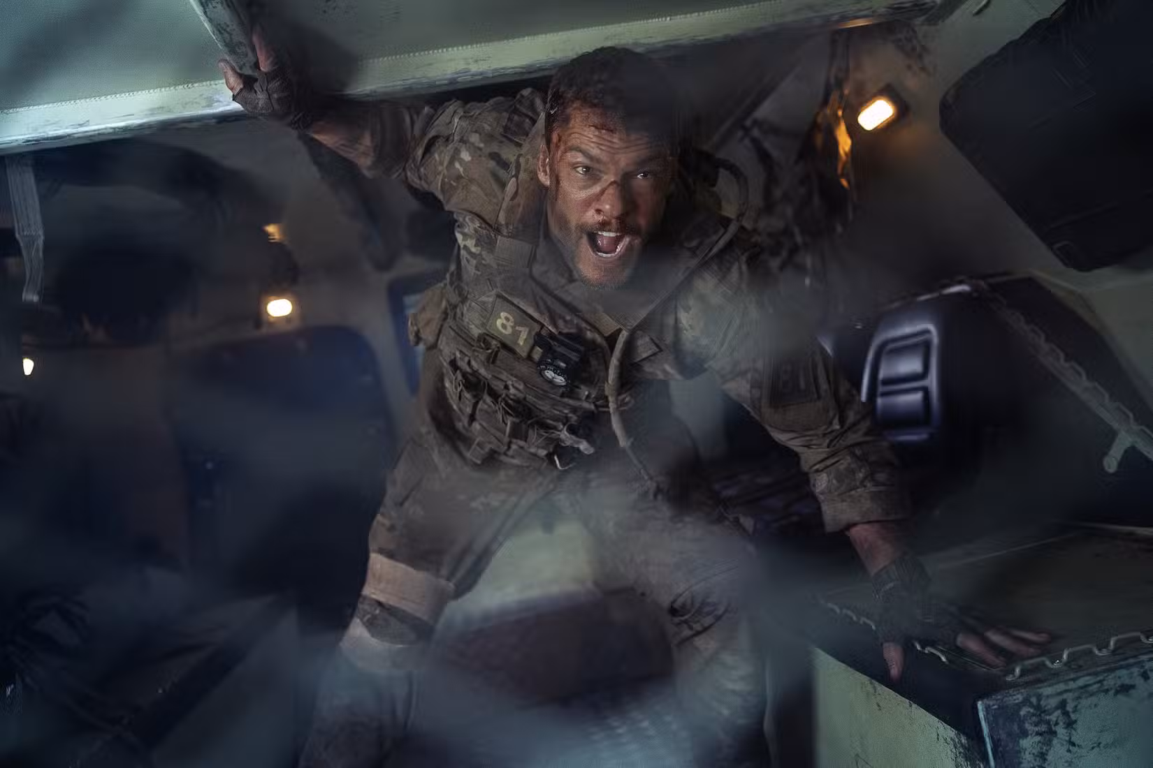 O sargento 81 do exército (Alan Ritchson) está na traseira de um transporte blindado e grita através de uma grade de metal em War Machine