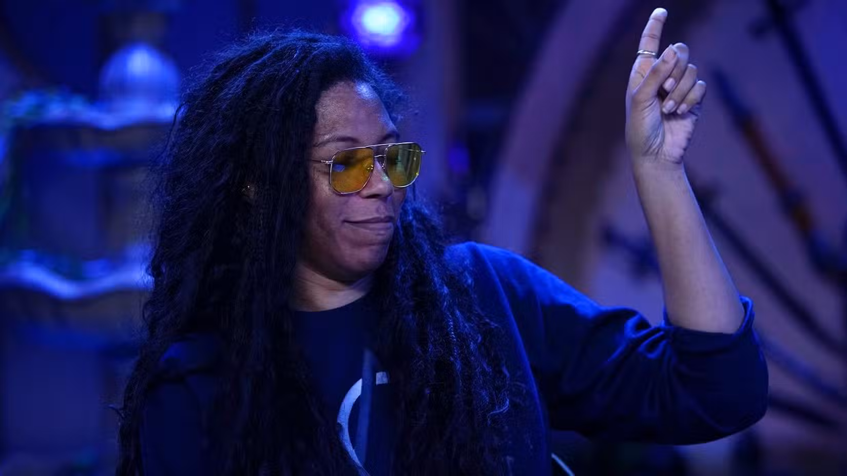 Uma imagem com Aabria Iyengar do Critical Role. Ela aponta para o ar com uma expressão satisfeita no rosto.