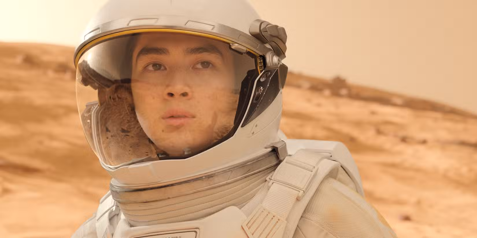 Uma imagem da 5ª temporada de For All Mankind da Apple TV. Ela mostra uma mulher em um traje de astronauta com um fundo avermelhado (supostamente o planeta Marte) atrás dela.